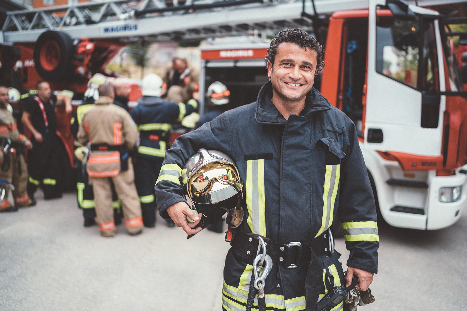 smiling fireman holding his helmet in front of fire truck