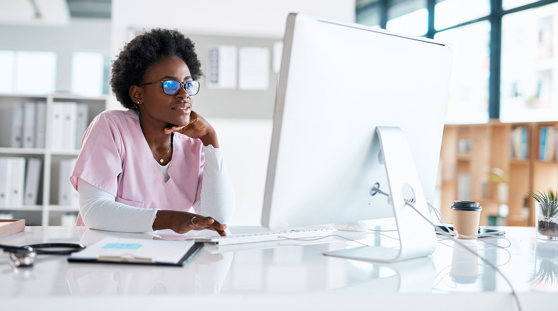 woman in pink scrubs at desk looking at computer monitor